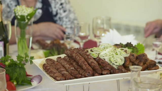Dinner table served with lula kebabs and fresh vegetables. People enjoy Armenian style kebab at restaurant.