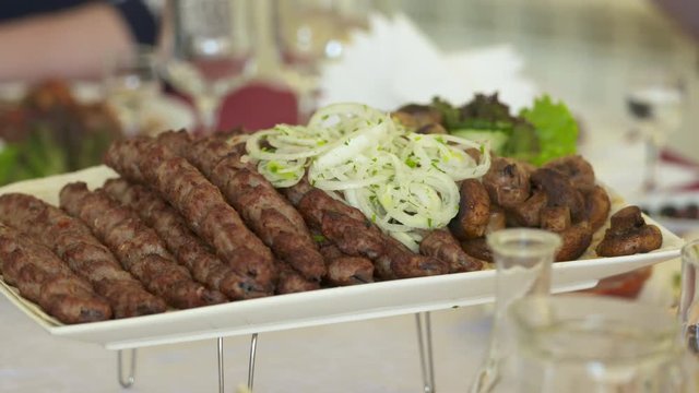 Dinner table served with lula kebabs and fresh vegetables. People enjoy Armenian style kebab at restaurant.