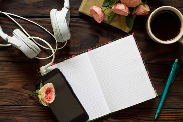 Smartphone, headphones and open notebook with blank pages next to cup of coffee on wooden table. Top view flat lay background.