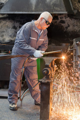 senior worker in protective mask welding steel railings outdoors