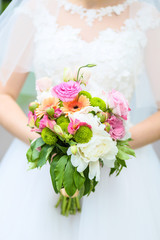 The bride is holding a beautiful wedding bouquet of peonies and orchids in her hands