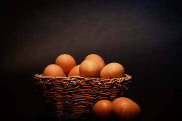 Brown eggs in and around a wicker basket on a dark background.