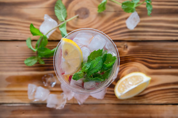 Glass of water with lemon and mint served with ice cubes on a wooden board