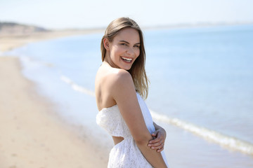Fototapeta na wymiar Junge blonde Frau steht lachend an einem Strand