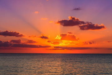 Sunset on the Caribbean sea. The sunset photo has been taken from island Cozumel - Mexico. The sky is blue with a yellow - purple sun on the horizon. Sun rays of light escaping through the clouds.