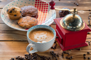 Red coffee mill, cup latte with a painted cat on milk foam and biscuits on a old wooden table.