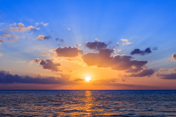 Sunset on the Caribbean sea. The sunset photo has been taken from island Cozumel - Mexico. The sky is blue with a yellow - purple sun on the horizon. Sun rays of light escaping through the clouds.