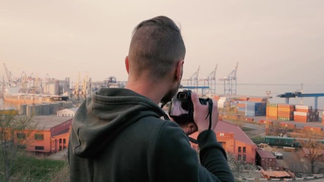 young male photographer filming industrial zone, cargo sea port background