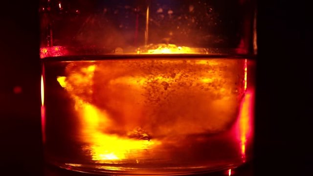 Selective focus pure whisky with ice cube inside whisky glass on dark foggy background alcohol drink concept. Close up. Slider shot