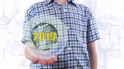 Young man shows a hologram of the planet Earth and text 2019. Boy with future technology 3d projection on a modern white digital background - Powered by Adobe