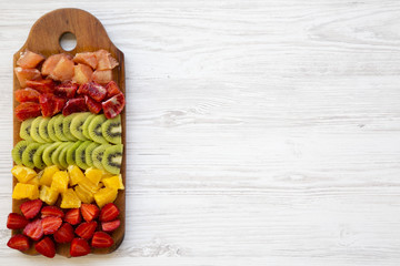 Chopped fresh fruits arranged on cutting board on white wooden background with copy space, top view. Ingredients for fruit salad. From above, flat lay, overhead.