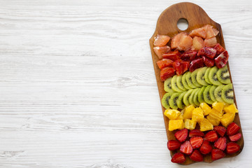 Chopped fresh fruits arranged on cutting board on white wooden background with copy space, top view. Ingredients for fruit salad. From above, flat lay, overhead.