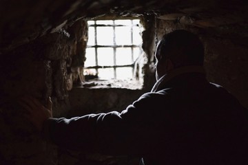 Fototapeta premium Man prisoner watching out from underground window, hands on the wall