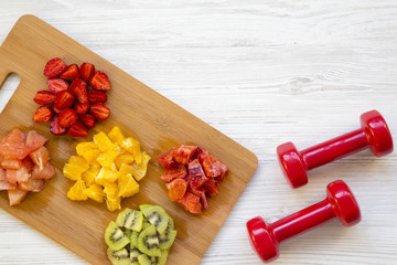 Chopped colorful raw fruits and dumbbells on white wooden background, top view. Copy space.
