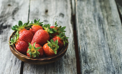 Fresh strawberries in a wooden bowl on a rustic wooden table