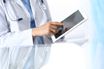 Woman doctor using tablet computer while sitting. Reflecting glass table is a working place of physician. Healthcare, insurance and medicine concept