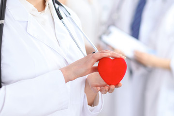 Female doctor holding heart in her hands.  Doctor and patient sitting in the background. Cardiology...