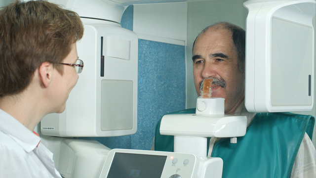 Dentist talking to a senior patient before examination by using panoramic and cephalometric X-Ray scanner - Powered by Adobe