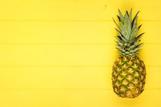 Pineapple on a bright bold yellow wood background. Minimal summer concept. Top view. Copy space.