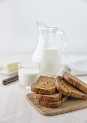 Bread on a cutting board with a glass jug of milk and a glass and cheese on a small plate. Selective focus. Blur