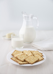 Fototapeta na wymiar Crackers on a white plate with a glass jug of milk and a glass and cheese on a small plate Selective focus. Blur