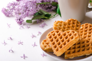 Homemade waffles heart on plate on a white table with flowers. Sweet pastry.