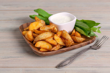 Slices of baked potatoes with leeks and garlic sauce in a wooden bowl