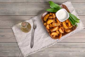Slices of baked potatoes with leeks, garlic sauce and olive oil in a wooden bowl on a rustic background