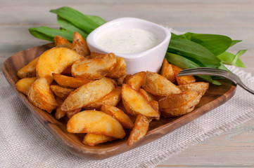 Slices of baked potatoes with leeks and garlic sauce in a wooden bowl