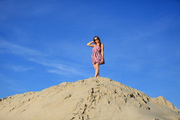 Piękna rudowłosa dziewczyna stoi na szczycie piaszczystej wydmy.