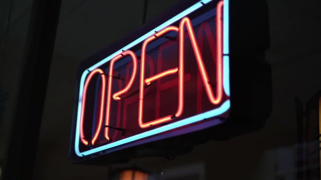 Open sign in window of local shop establishing shot.
