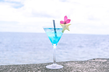 Blue cocktail in a martini glass with pink flower garnish and star fruit, plus plastic straws and ocean in background, at Apia, Upolu Island, Samoa, South Pacific