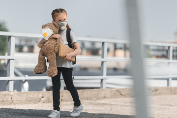 Fototapeta premium kid in protective mask walking with teddy bear and book on bridge, air pollution concept