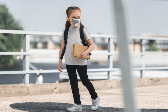 kid in protective mask walking with book on bridge, air pollution concept
