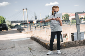 child in protective mask using tablet, air pollution concept