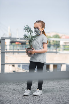 Child In Protective Mask Holding Green Potted Plant, Air Pollution Concept