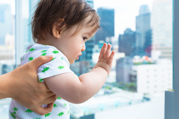 Toddler boy looking out at Downtown Los Angeles from a glass balcony