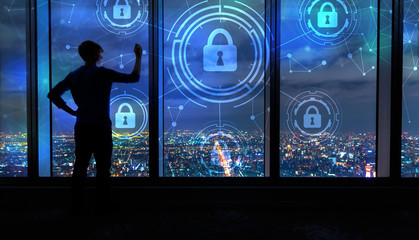 Cyber Security with man writing on large windows high above a sprawling city at night