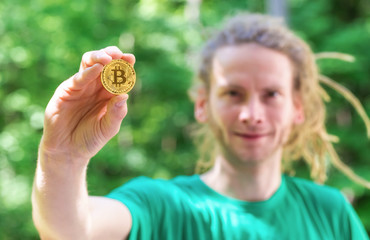 Man holding a physical bitcoin cryptocurrency in his hand outside