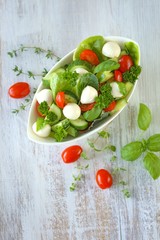 Vegetable  salad from tomatoes, cucumbers, mozzarella, parsley, basil in white cups on a white shabby wooden background.Vegetarian menu.Vegan food	