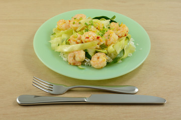 Shrimp and zucchini on rice on green plate with fork and knife on wooden table