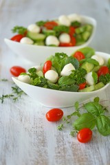 Vegetable summer salad from tomatoes, cucumbers, mozzarella, parsley, basil in white cups on a white shabby wooden background.Vegetarian menu.	