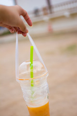 The woman's hand is holding a plastic cup of Thai tea, picture in blurred background