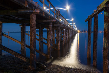 Lights of White Rock pier reflecting in ocean at night in blue hour