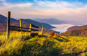 Obraz premium beautiful mountainous landscape with wooden fence. lovely autumnal scenery at sunrise with gorgeous sky over the valley full of fog