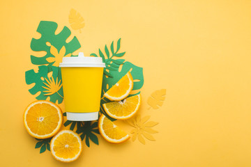 Colorful summer drink concept. Disposable paper cup on a yellow background with tropical leaves and...
