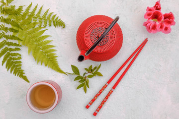 Asian food background, red tea pot, caps and chopsticks on grey concrete background. Top view, flat lay