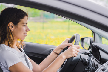 Young steering the car wheel, focused, smiling. Side view.