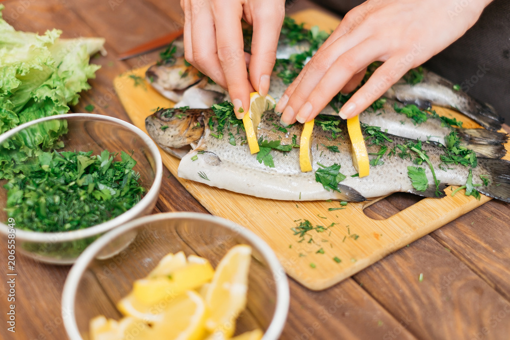 Wall mural woman preparing fish with lemons and greenery.