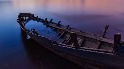 Old wooden boat with sunset on the beach.